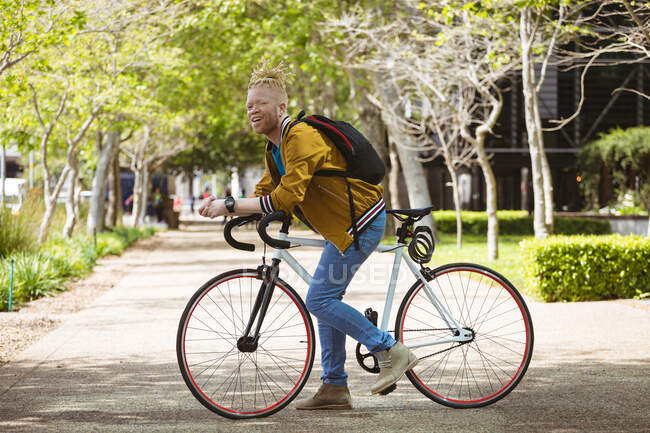 Портрет улыбающегося альбиноса африканского американца с дредами на велосипеде. on the go, out and about in the city. — стоковое фото