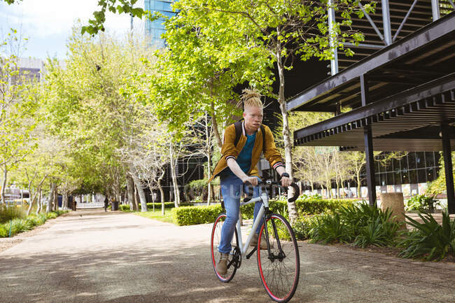 Pensiero albino uomo afroamericano con dreadlocks in sella alla bicicletta. in movimento, in giro per la città. — Foto stock