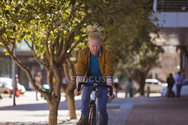 Nachdenklicher Albino-Afrikaner mit Dreadlocks auf dem Fahrrad. Unterwegs, unterwegs in der Stadt. — Stockfoto
