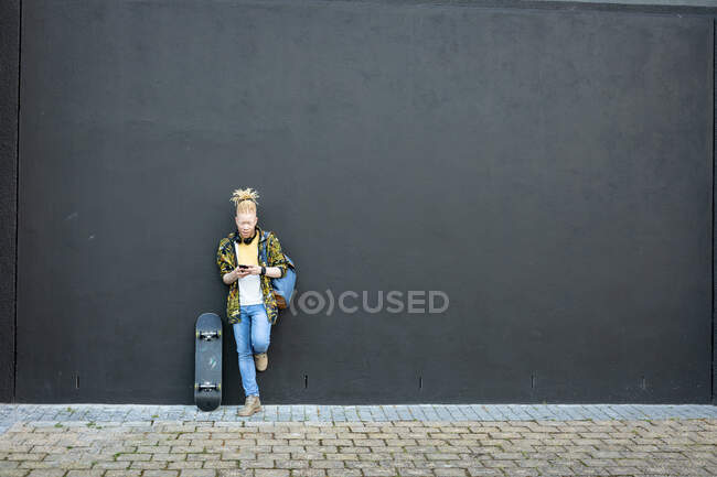 Задумчивый альбинос африканский американец с дредами, использующий смартфон. цифровая реклама на ходу, на улице и по городу. — стоковое фото