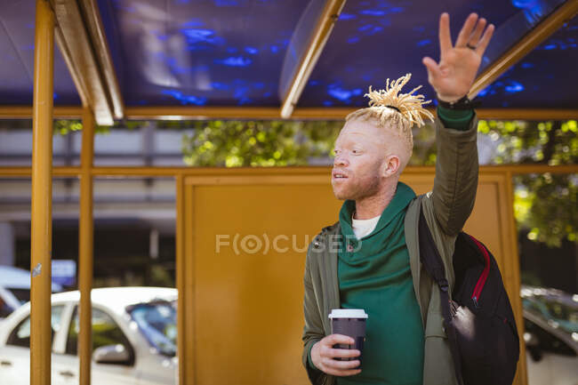 Homme afro-américain albinos avec dreadlocks tenant café à emporter et saluant. on the go, out and about dans la ville. — Photo de stock
