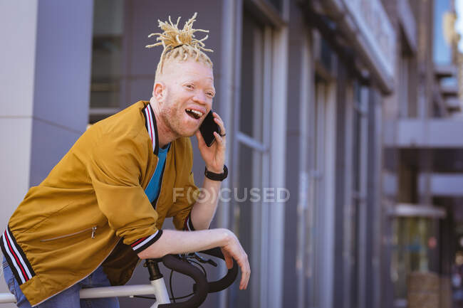 Feliz albino hombre afroamericano con rastas hablando en smartphone. nómada digital sobre la marcha, fuera y alrededor de la ciudad. - foto de stock