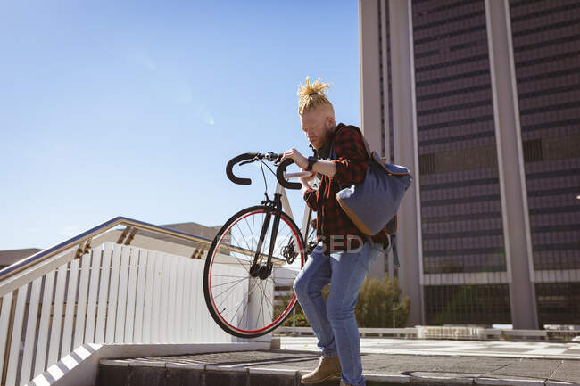 Homem americano albino afro-americano cuidadoso com dreadlocks descendo escadas com bicicleta. em movimento, fora e em torno da cidade. — Fotografia de Stock