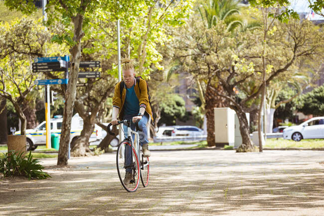 Задумчивый альбинос африканский американец с дредами на велосипеде. on the go, out and about in the city. — стоковое фото