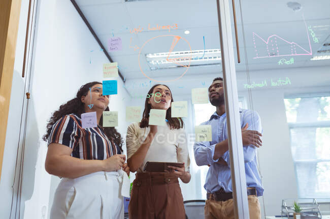 Três empresários diversos discutindo e tomando notas na parede de vidro no escritório moderno. empresa e escritório local de trabalho. — Fotografia de Stock