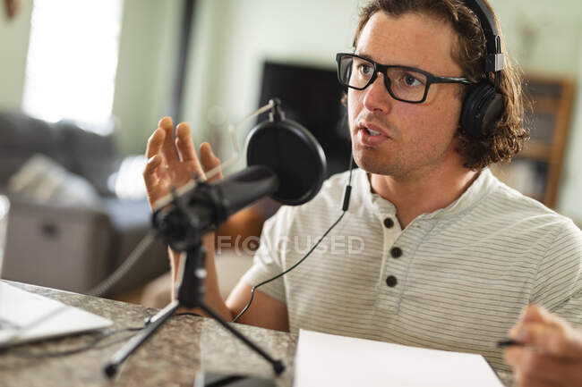 Uomo caucasico che registra podcast usando il microfono seduto a casa. blogging, podcast e tecnologia di trasmissione concetto — Foto stock