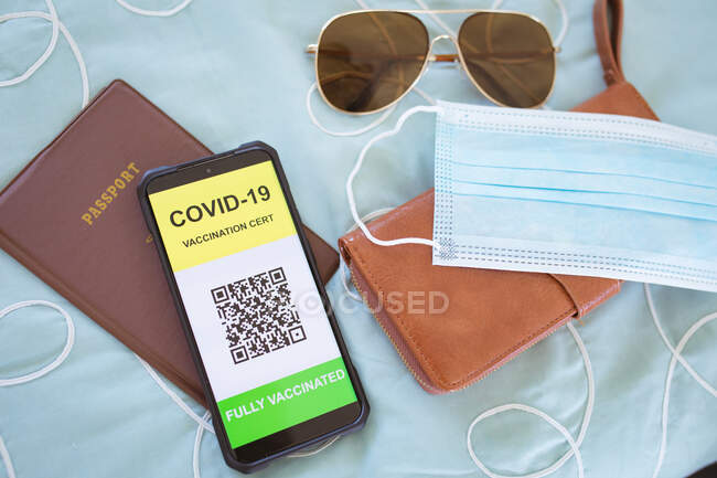 Glasses, face mask, documents and smartphone with covid 19 passport on screen lying on bed. travel preparation during covid 19 pandemic. — Stock Photo