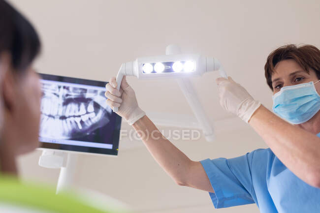 Infirmière dentaire blanche portant un masque facial tenant la lampe à la clinique dentaire moderne. soins de santé et de la dentisterie. — Photo de stock