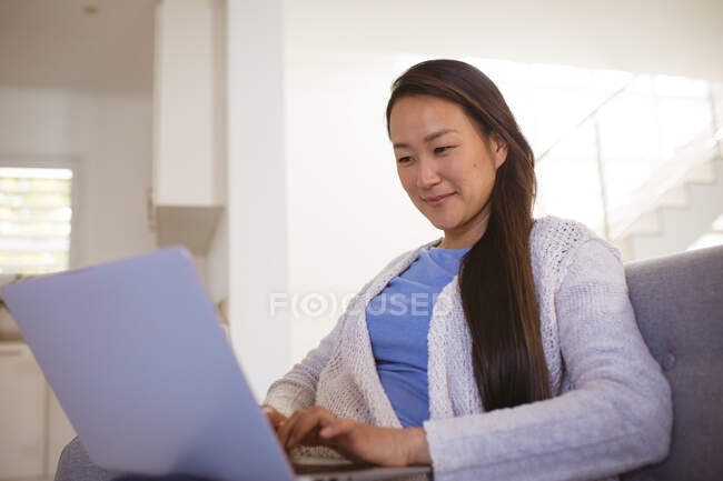 Щаслива азіатка сидить на дивані з ноутбуком вдома. спосіб життя і розслаблення вдома з технологіями . — стокове фото
