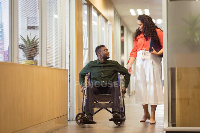 Empresário americano africano em cadeira de rodas conversando com empresária birracial no escritório moderno. empresa e escritório local de trabalho. — Fotografia de Stock