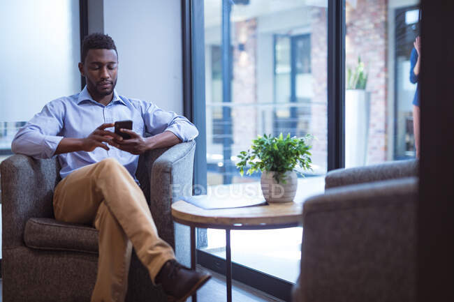 Homme d'affaires afro-américain utilisant un smartphone dans un bureau moderne. lieu de travail professionnel et de bureau. — Photo de stock