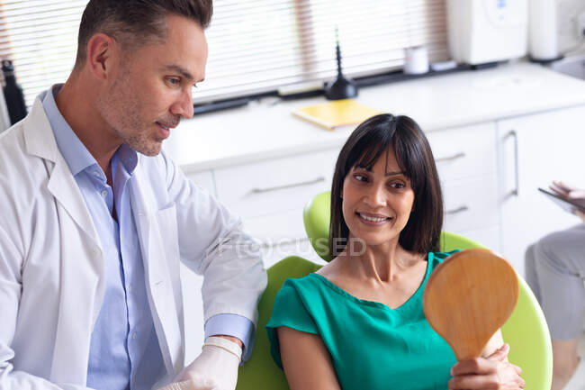 Smiling caucasian male dentist with female patient looking at mirror at modern dental clinic. — Stock Photo