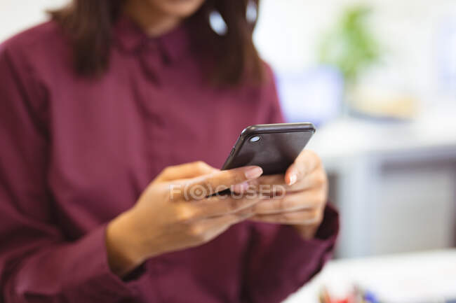 У середній частині біржової ділової жінки, яка сидить на столі за допомогою смартфона в сучасному офісі. на роботі та в офісі. — стокове фото