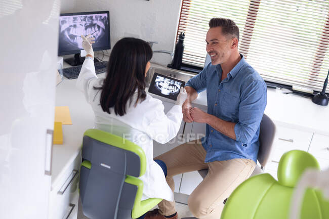 Odontóloga birracial sonriente que examina los dientes de un paciente masculino en una clínica dental moderna. negocio de salud y odontología. - foto de stock