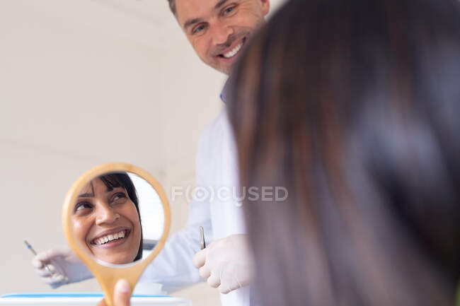 Dentista masculino caucasiano sorridente com paciente olhando para o espelho na clínica odontológica moderna. serviços de saúde e odontologia. — Fotografia de Stock