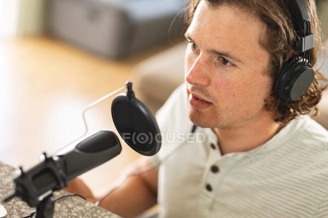 Homem caucasiano gravando podcast usando microfone sentado em casa. conceito de tecnologia de blogging, podcast e radiodifusão — Fotografia de Stock