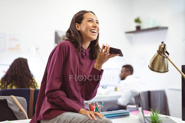 Щаслива бізнес-леді розмовляє по смартфону з колегами на задньому плані в сучасному офісі. бізнес та офісне робоче місце . — стокове фото