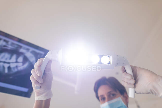 Белая женщина-стоматолог в маске для лица держит лампу в современной стоматологической клинике. здравоохранение и стоматология. — стоковое фото