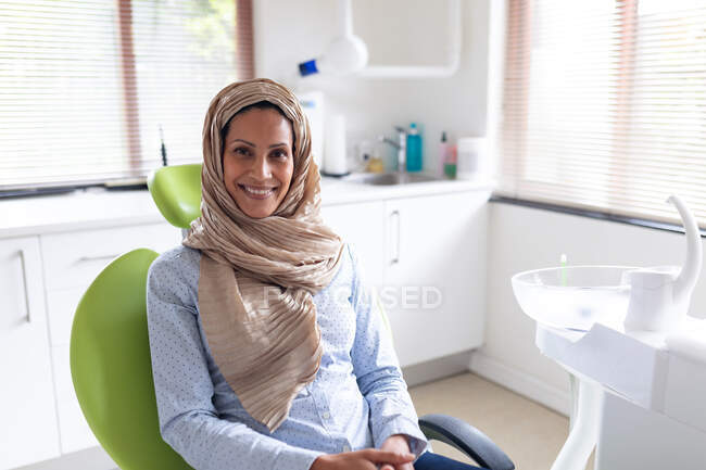Portrait d'une patiente souriante biraciale assise dans une clinique dentaire moderne. soins de santé et de la dentisterie. — Photo de stock