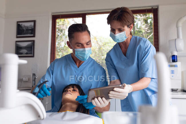 Il dentista maschio caucasico e l'infermiera dentale femminile esaminano i denti del paziente presso la moderna clinica dentale. attività sanitaria e odontoiatrica. — Foto stock