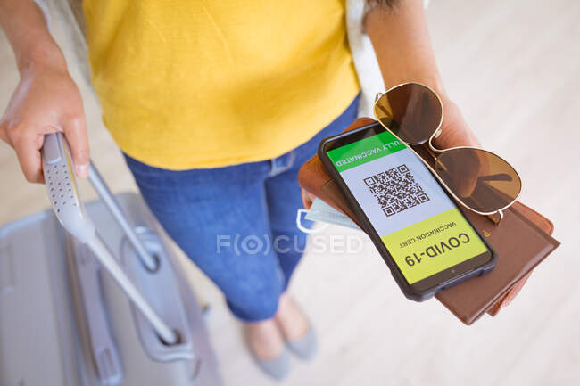 Hände einer Frau mit Dokumenten und Smartphone mit gefälschtem Reisepass auf dem Bildschirm. Reisevorbereitung während Covid 19 Pandemie. — Stockfoto