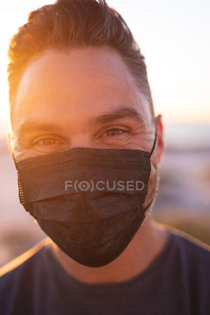Portrait d'un homme caucasien portant un masque facial regardant une caméra au bord de la mer. route d'été et vacances dans la nature pendant la pandémie covid 19. — Photo de stock