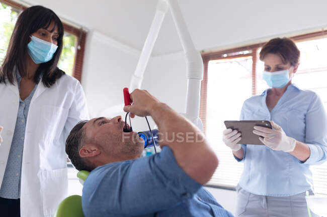 Odontoiatra biennale con infermiera che esamina i denti di un paziente di sesso maschile presso una moderna clinica dentale. attività sanitaria e odontoiatrica. — Foto stock