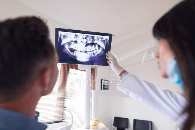 Odontoiatra biennale con maschera facciale che esamina i denti di un paziente di sesso maschile presso una moderna clinica dentale. attività sanitaria e odontoiatrica. — Foto stock