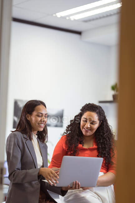Duas mulheres de negócios sorrindo diversas que sentam-se e usam o computador portátil no escritório moderno. empresa e escritório local de trabalho. — Fotografia de Stock
