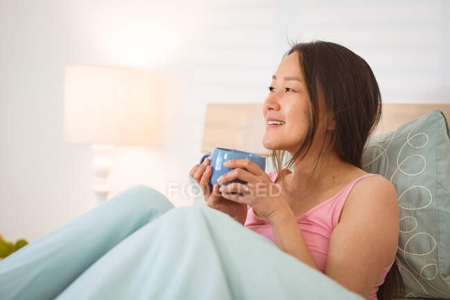 Mulher asiática feliz deitada na cama, bebendo café pela manhã. estilo de vida, passar o tempo e relaxar em casa. — Fotografia de Stock