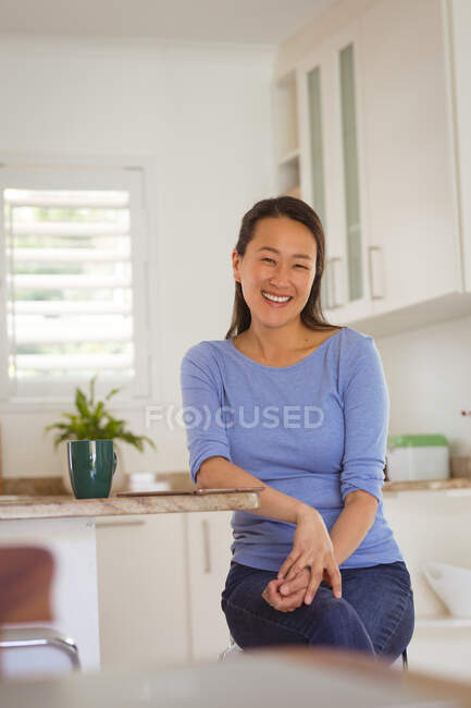 Mujer asiática feliz sentada en la mesa en la cocina. estilo de vida, ocio y pasar tiempo en casa. - foto de stock