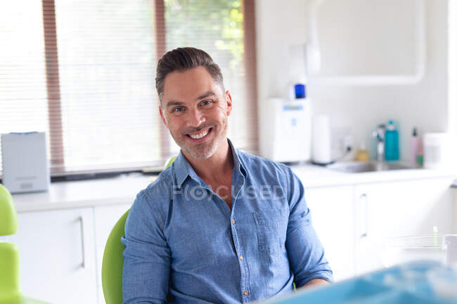 Portrait of smiling caucasian male patient looking at camera at modern dental clinic. healthcare and dentistry business. — Stock Photo