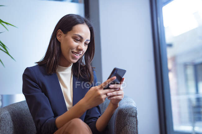 Бірасовий бізнес-леді посміхається і розмовляє по смартфону, сидячи в сучасному офісі. бізнес та офісне робоче місце . — стокове фото