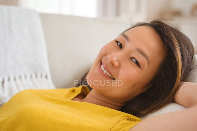 Портрет щасливої азіатки лежить на дивані і відпочиває, дивлячись на камеру. Спосіб життя, відпочинок і перебування вдома. — стокове фото