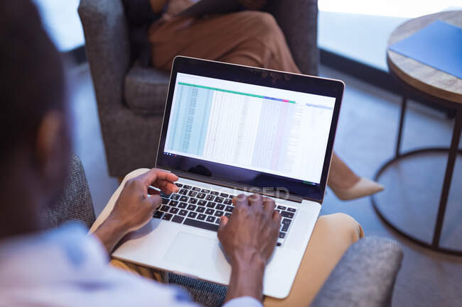 Empresário afro-americano usando laptop com colegas em segundo plano no escritório moderno. empresa e escritório local de trabalho. — Fotografia de Stock