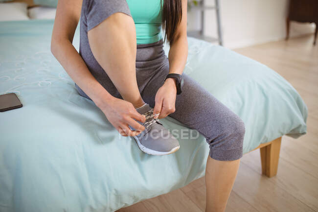 Midsection of woman sitting on bed in fitness clothes, preparing for exercise, tying shoes. healthy active lifestyle and fitness at home. — Stock Photo