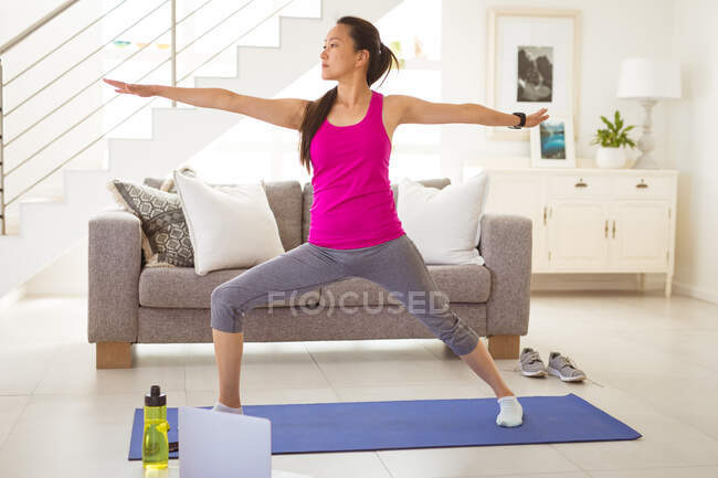 Зосереджена азіатська жінка на килимку, практикує йогу вдома з ноутбуком. здоровий активний спосіб життя і фізична підготовка вдома з технологіями . — стокове фото