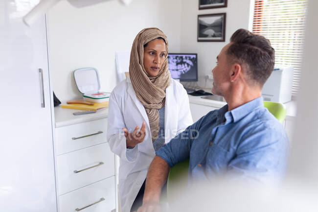 Двухсторонняя женщина-стоматолог говорит и осматривает зубы пациента мужского пола в современной стоматологической клинике. здравоохранение и стоматология. — стоковое фото