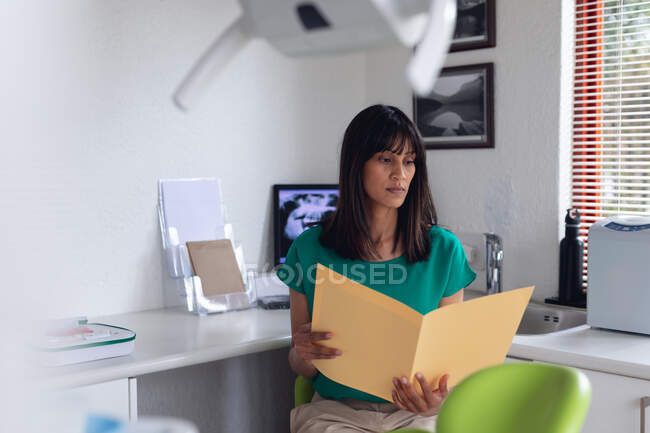 Nachdenkliche zweirassige Patientin beim Betrachten von Dokumenten in einer modernen Zahnklinik. Gesundheits- und Zahnarztgeschäft. — Stockfoto