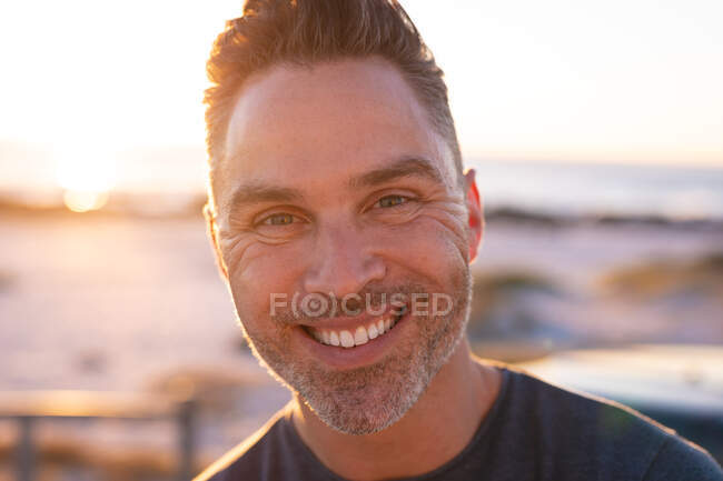 Porträt eines lächelnden kaukasischen Mannes, der am Meer in die Kamera blickt. Sommer Roadtrip und Urlaub in der Natur. — Stockfoto