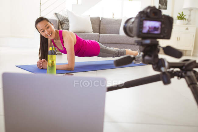 Щаслива азіатська жінка вправляється на килимку, роблячи фітинги відеоблог з дому. здоровий активний спосіб життя і фізична підготовка вдома з технологіями . — стокове фото