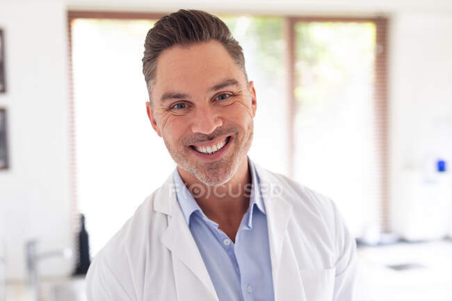 Портрет улыбающегося кавказского стоматолога, смотрящего в камеру в современной стоматологической клинике. здравоохранение и стоматология. — стоковое фото