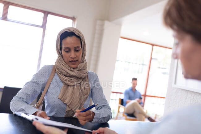 Femme de naissance signant des documents sur presse-papiers à la réception à la clinique dentaire moderne. soins de santé et de la dentisterie. — Photo de stock