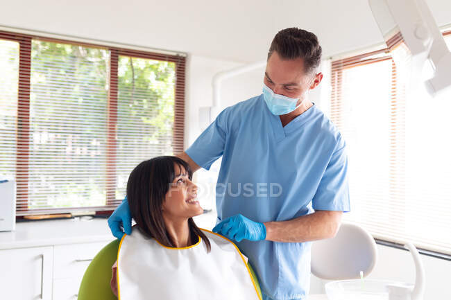 Dentista masculino caucásico que usa mascarilla para preparar a una paciente en una clínica dental moderna. negocio de salud y odontología. - foto de stock