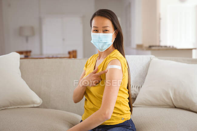 Mujer asiática feliz en mascarilla que muestra brazo con yeso después de la vacunación. salud y estilo de vida durante la pandemia de covid 19. - foto de stock