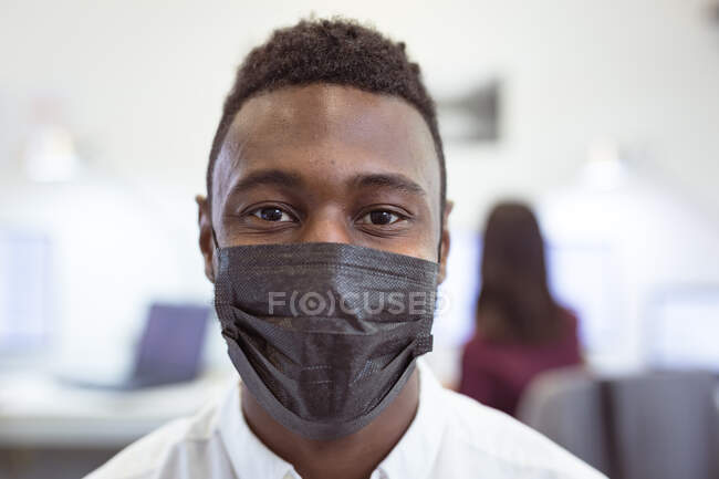 Retrato do empresário afro-americano usando máscara facial olhando para a câmera no escritório moderno. empresa e escritório local de trabalho durig covid 19 pandemia. — Fotografia de Stock