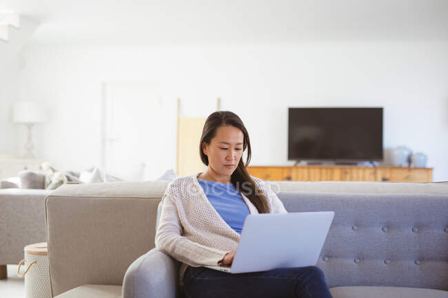 Felice donna asiatica seduta sul divano con computer portatile a casa. stile di vita e relax a casa con la tecnologia. — Foto stock