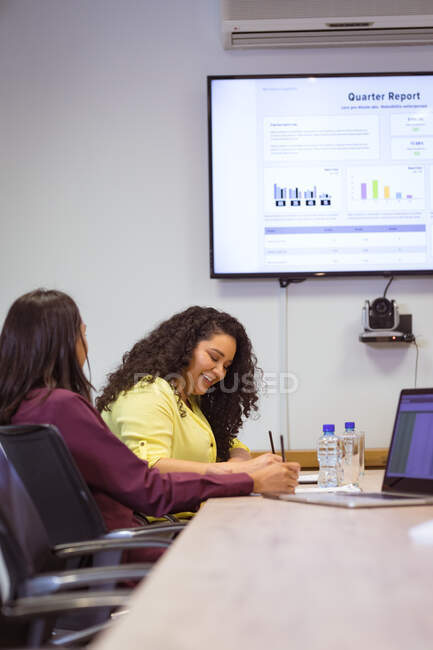 Две разные деловые женщины сидят за столом и делают заметки на встрече в современном офисе. деловые и офисные рабочие места. — стоковое фото