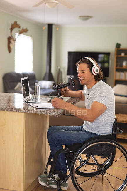 Uomo disabile caucasico che registra podcast usando il microfono seduto a casa. blogging, podcast e tecnologia di trasmissione concetto — Foto stock
