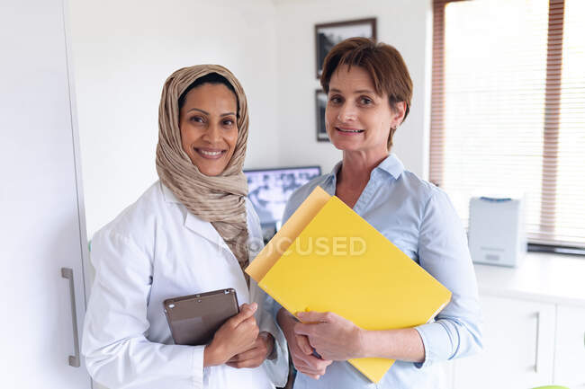 Portrait of smiling biracial female dentist and female dental nurse at modern dental clinic. healthcare and dentistry business. — Stock Photo